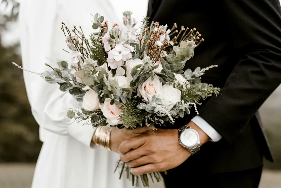 couple de mariés qui se tient la main en tenant un bouquet de fleurs