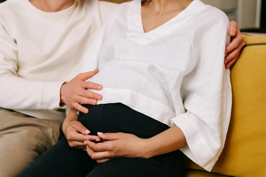 femme enceinte assise qui se tient le ventre et son conjoint qui touche son ventre