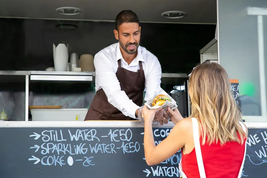 man in a foodtruck serving a burger to a girl with a red shirt