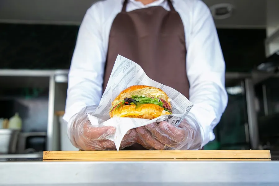 Chef holding a burger in his hands covered by plastics gloves